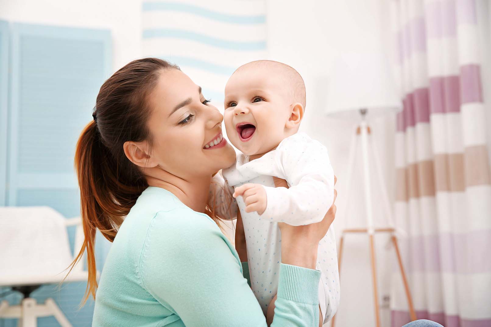 Mulher sorri para um bebê, segurando-o no colo.