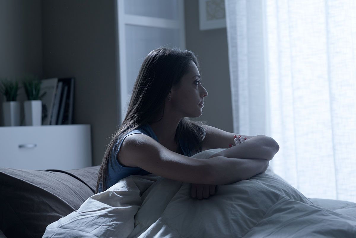 Mulher pensativa na cama: o que é depressão?