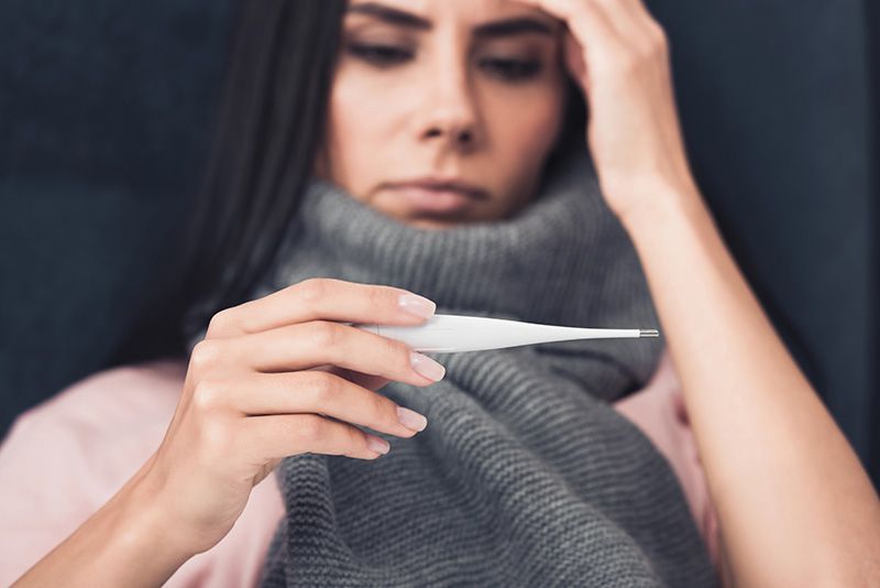 Mulher com gripe olha para termômetro