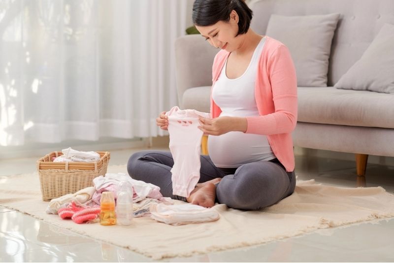 Gestante sentada no chão da sala segura alegre uma roupa para bebês